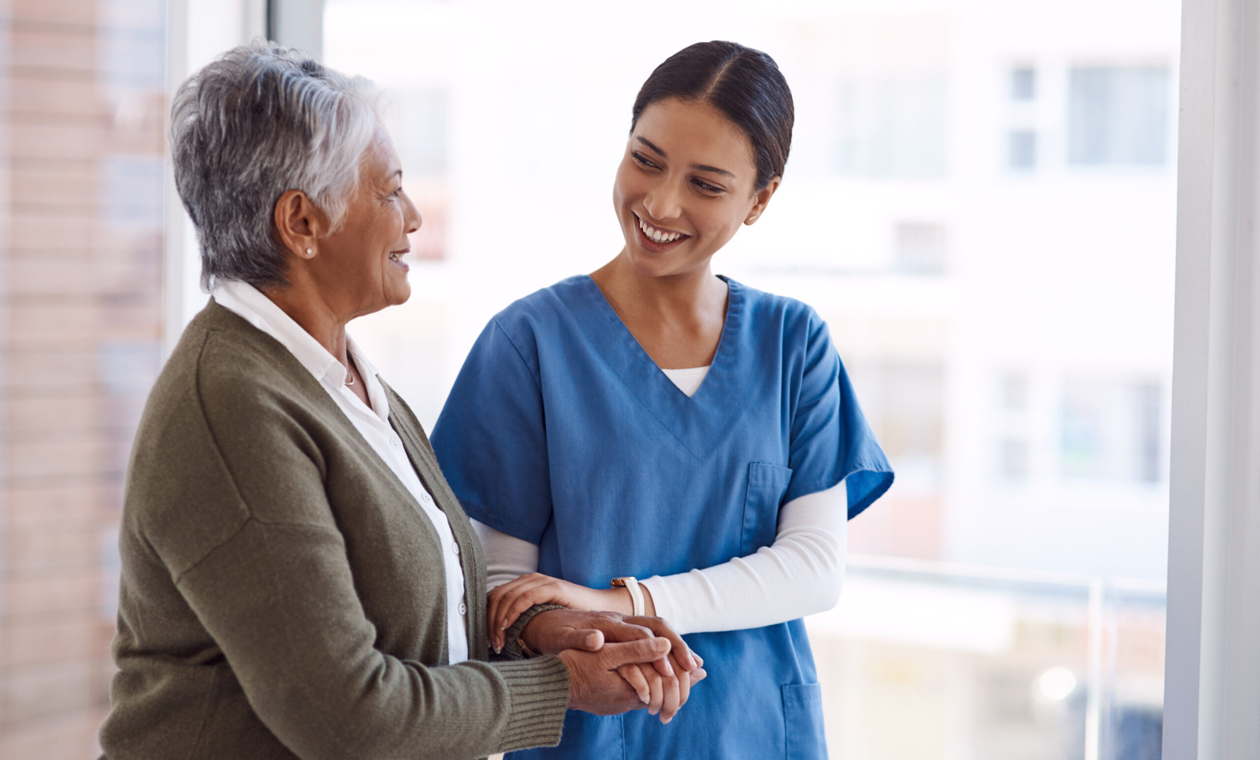 An elderly woman and nurse holding hands.