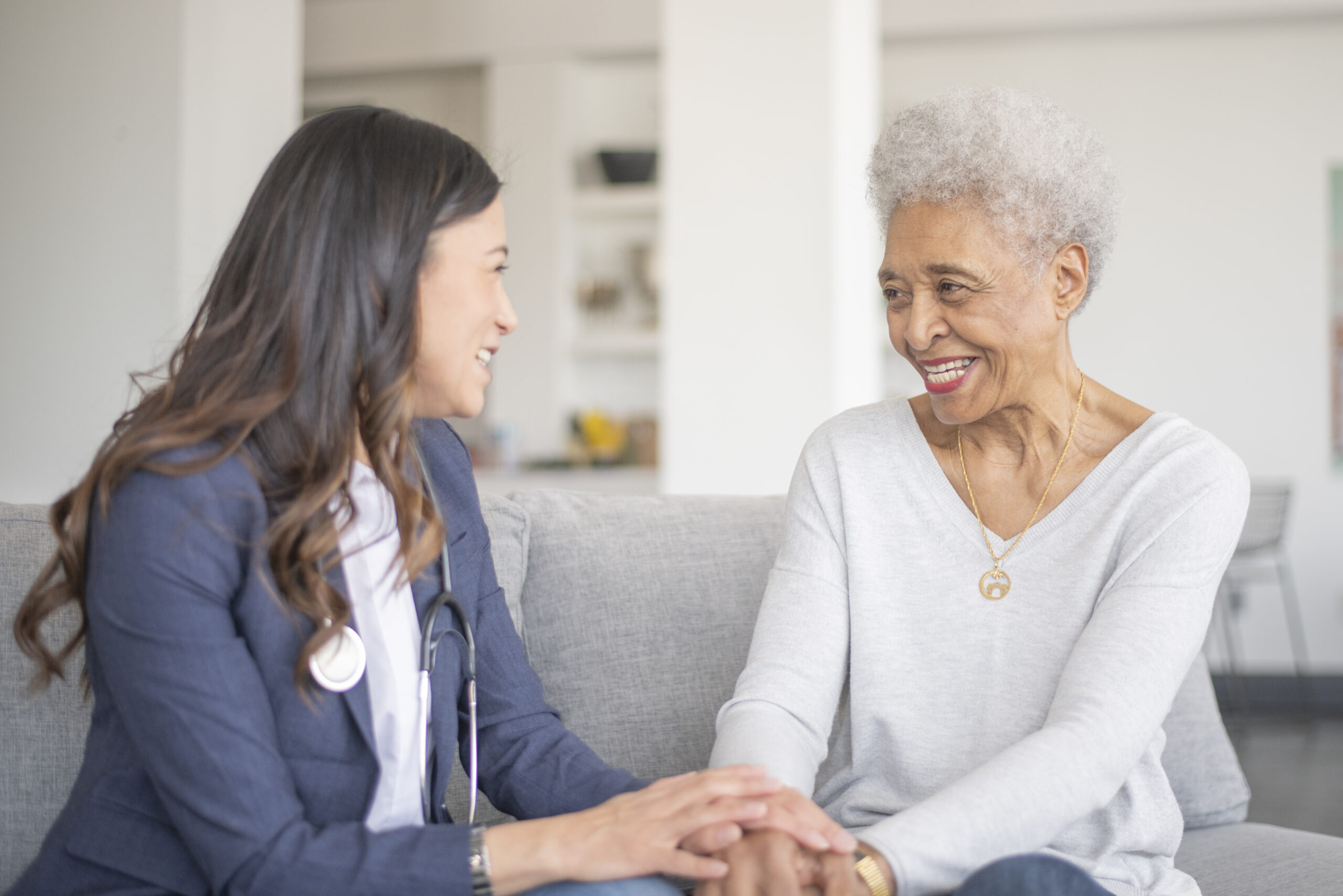 A healthcare professional and an older person smiling and talking on a sofa.