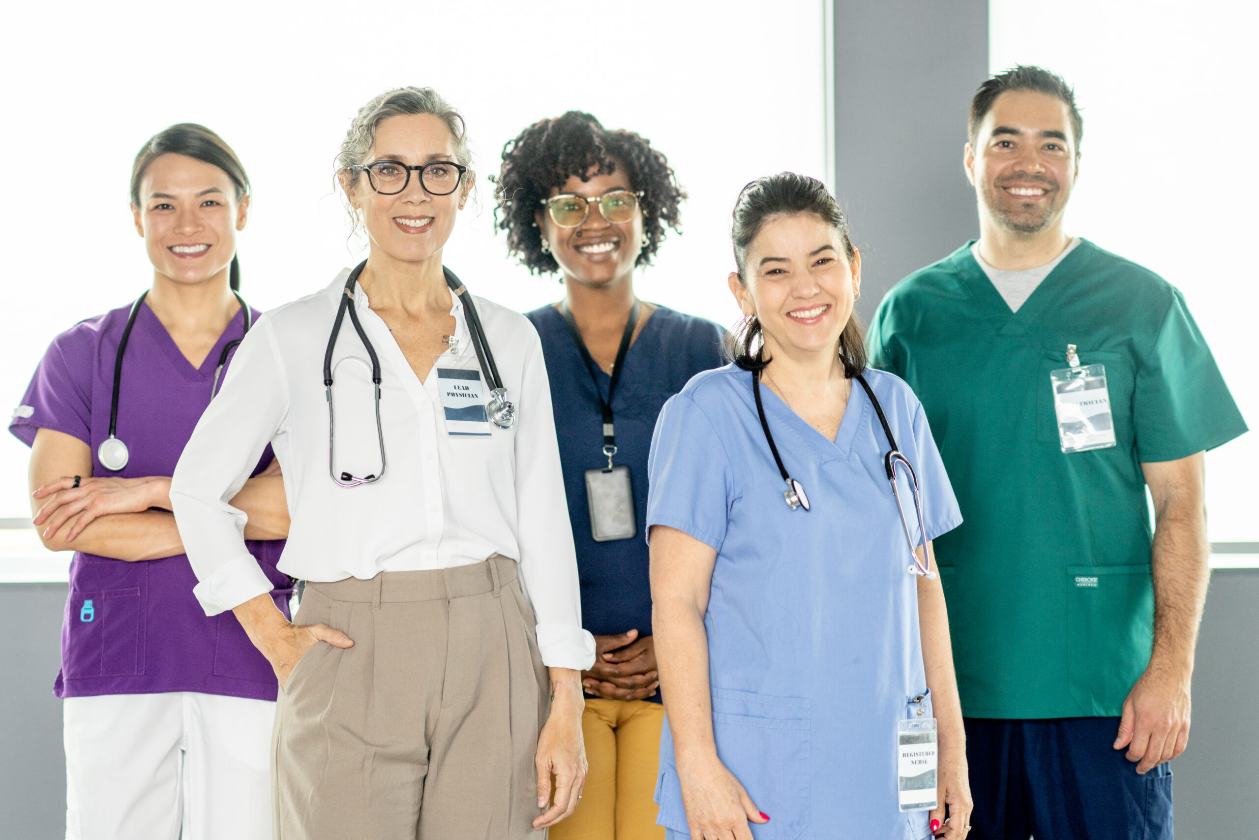 Medical Team of Professionals Smiling in a Modern Healthcare Facility A group of five diverse medical professionals in various colored uniforms, smiling.