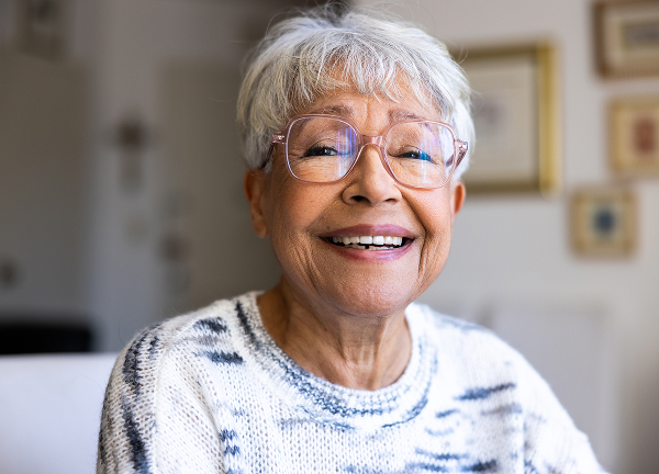 istockphoto-1472635214-612x612 An older person with white hair and glasses, smiling, wearing a patterned sweater indoors.
