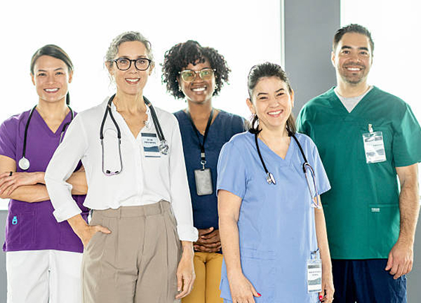 istockphoto-475374721-612x612 A group of five diverse medical professionals in various colored uniforms, smiling.